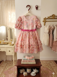 Floral dress with pink ribbon hanging on a hook in a room with a vanity and other dresses.